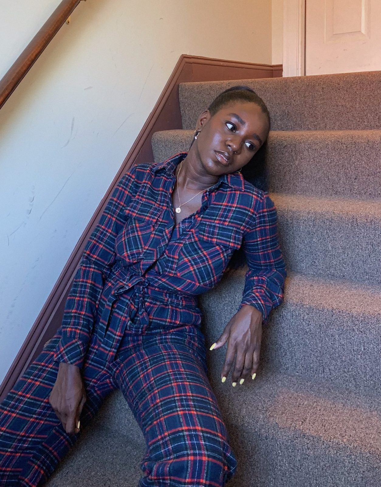 black girl wearing grunge blue and purple plaid utility jumpsuit on carpet stairs in hallway