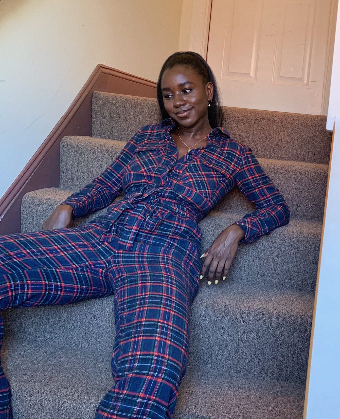 black girl wearing grunge blue and purple plaid utility jumpsuit on carpet stairs in hallway